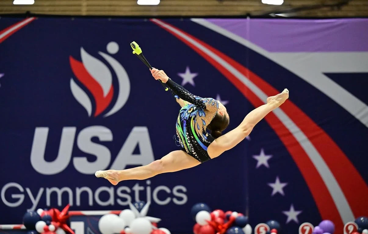 Gymnast performing a split leap with clubs at a USA Gymnastics event